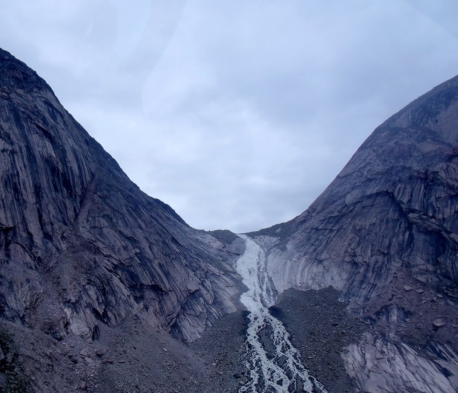 A meltwater stream braiding down a stark glacial valley between granite walls in Auyuittuq