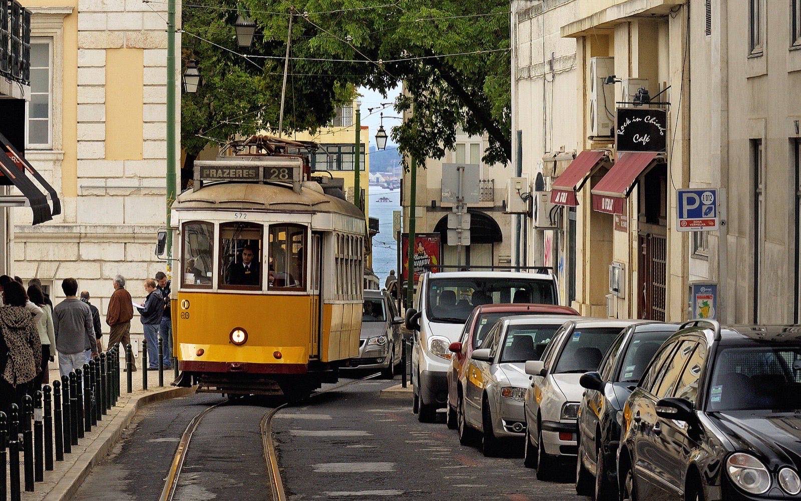 A yellow number 28 tram squeezing through a narrow Lisbon street