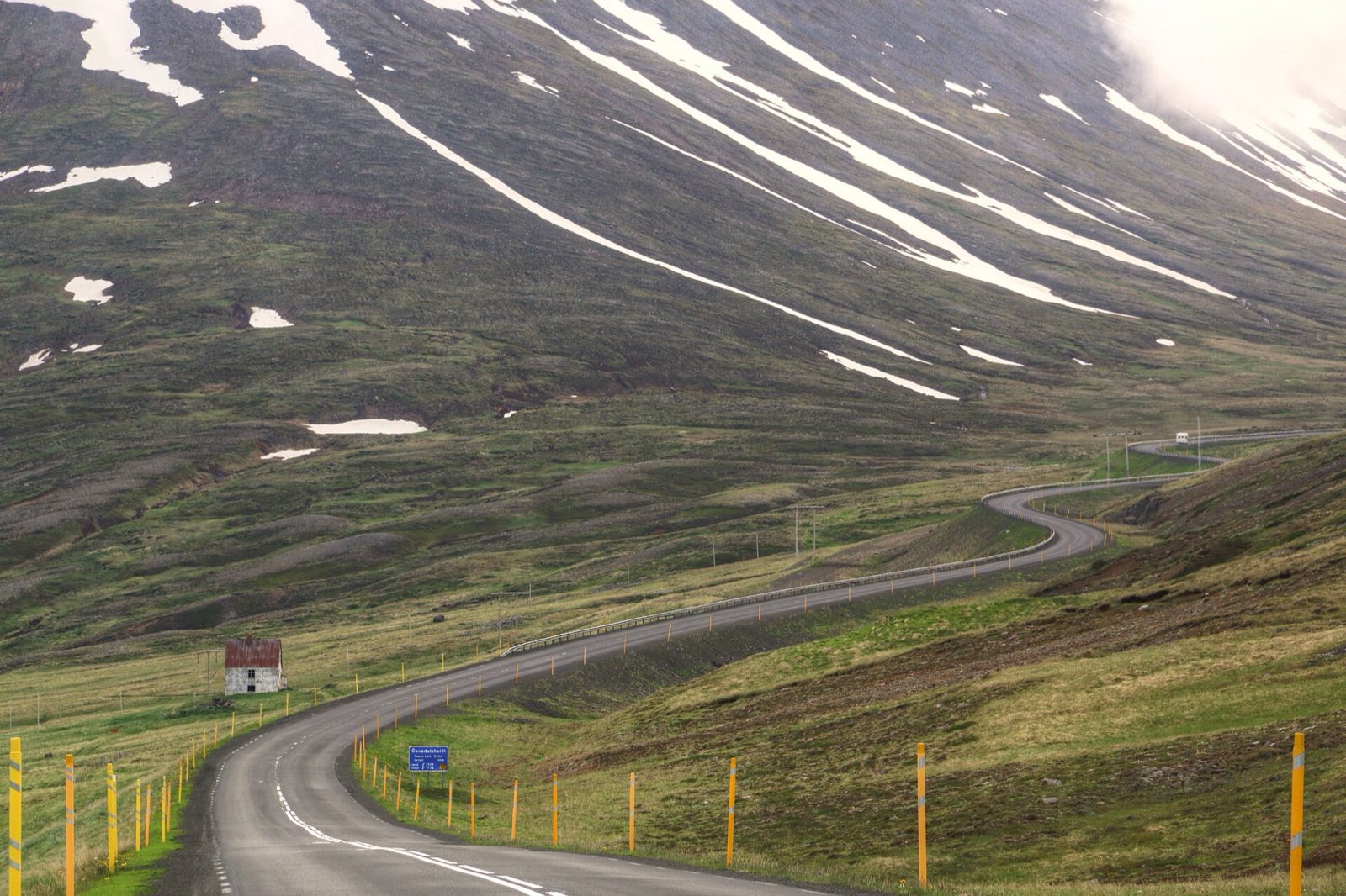 A two-lane road curving below snow-streaked mountainsides in northern Iceland