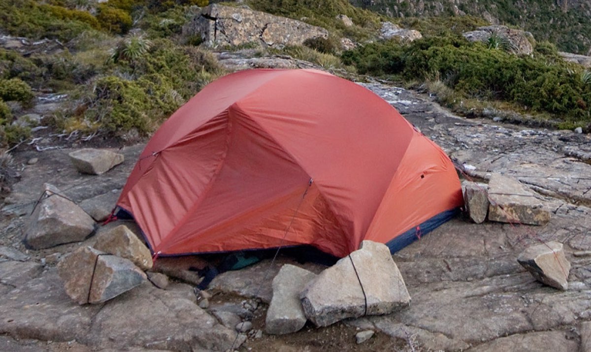 A tent pitched at a designated campsite with mountains behind