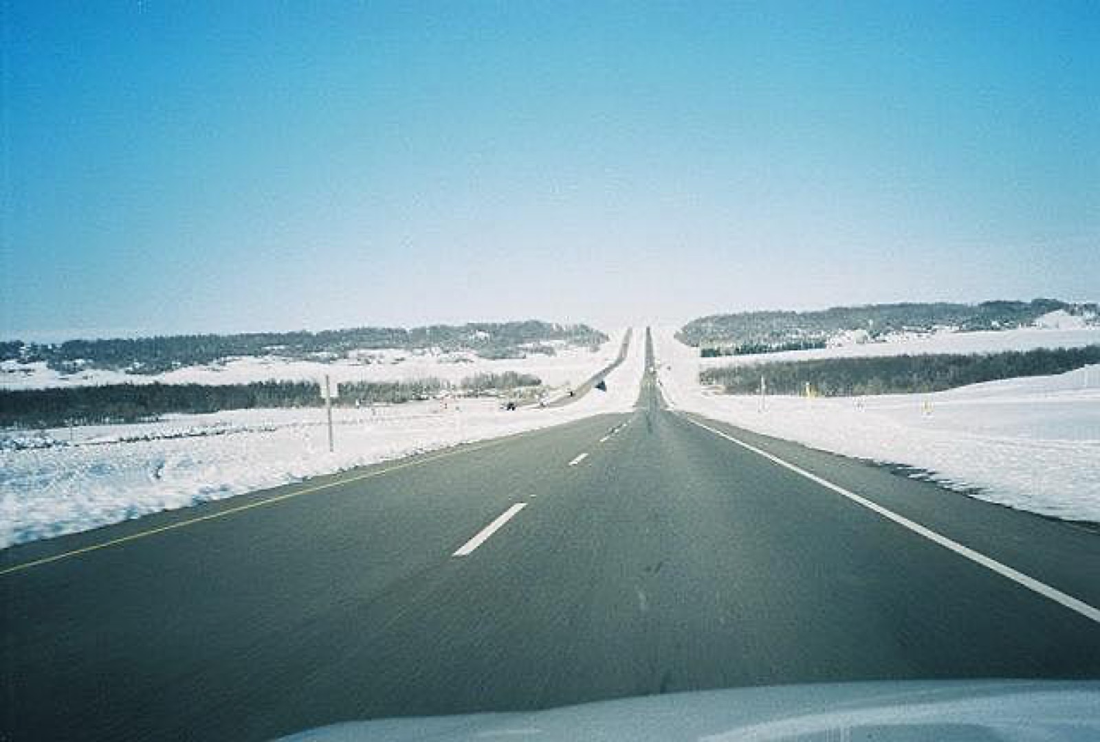 A driver's view of a snow-banked prairie highway stretching to the horizon